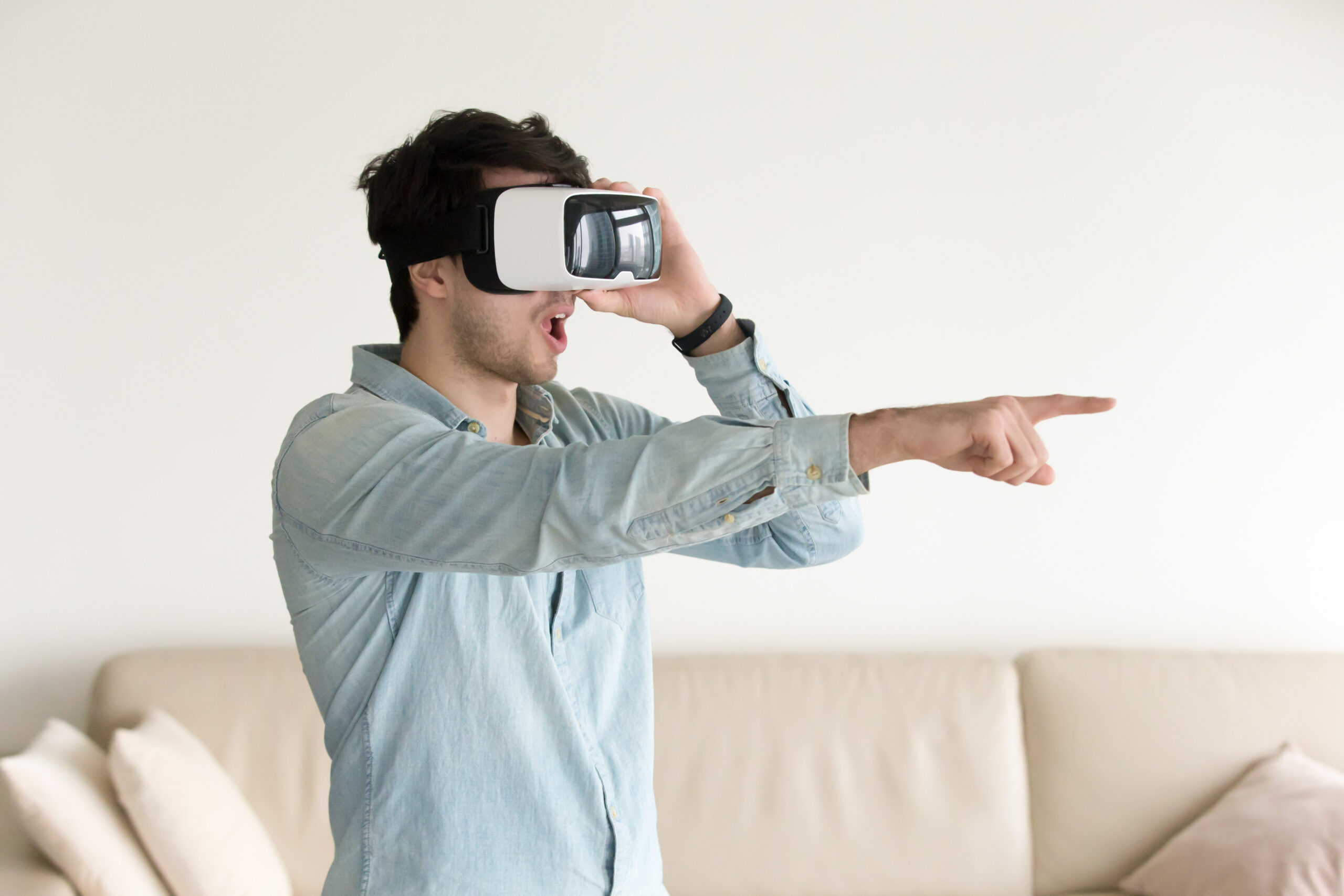 Surprised man using VR headset pointing at objects in augmented reality, wondering helmet innovative abilities, amazed young guy enjoying playing virtual games, watching 360 degree videos